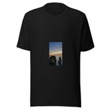 Maglietta unisex nera vista di fronte. Due scogli emergono dal mare: quello a sinistra è attraversato da un arco, mentre sopra l’orizzonte arancio vola la piccola sagoma di un aereo. Mockup del capo completo.