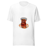 Maglietta unisex bianca vista di fronte. Tè ambrato scuro riempie un bicchiere sagomato, appoggiato su un piattino crema con decori corallo. Mockup del capo completo.